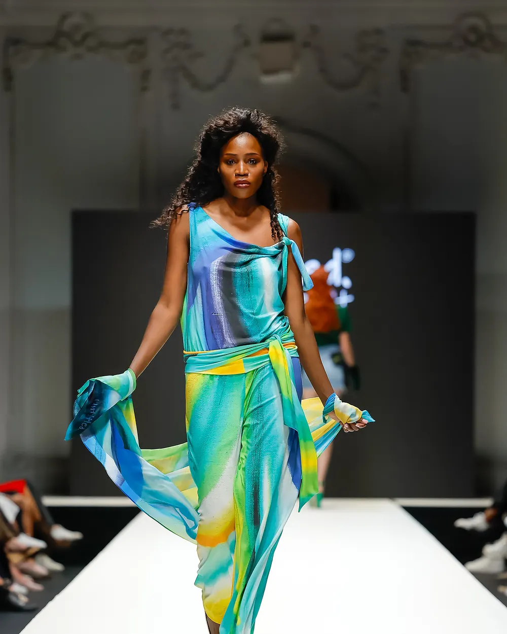 Model in einem fließenden Kleid mit türkis-grünem Farbverlauf