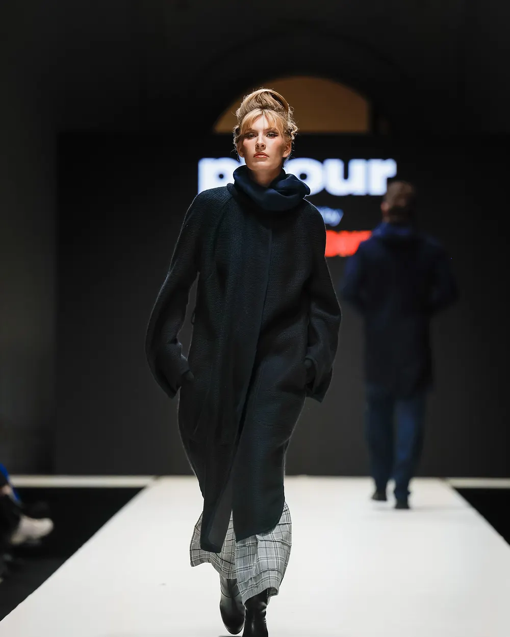 Model in dunklem, weit geschnittenem Mantel vor dem Schriftzug Pitour