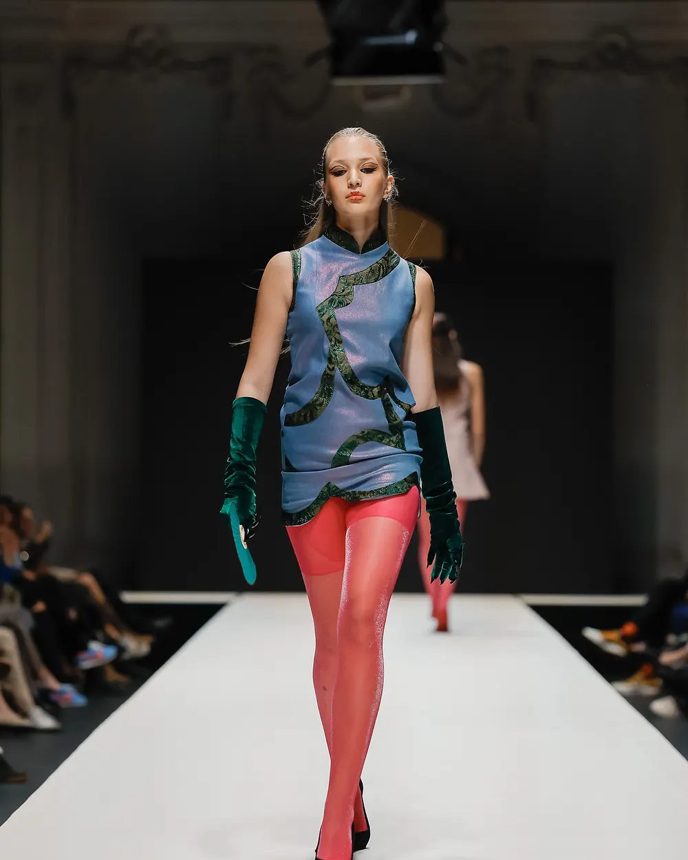 Model in blaugrünem Kleid mit langen grünen Handschuhen und roter Strumpfhose