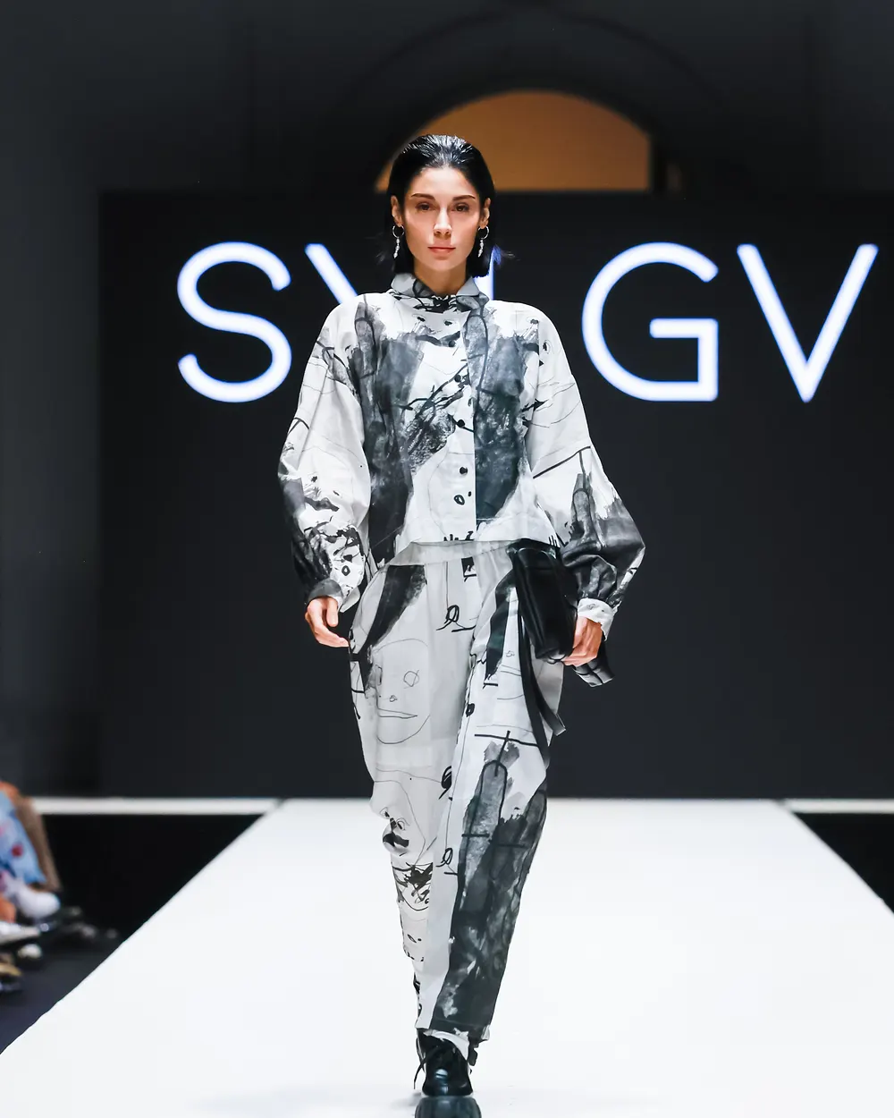 Model in schwarz-weiß bedrucktem Ensemble vor dem Schriftzug SYLGV